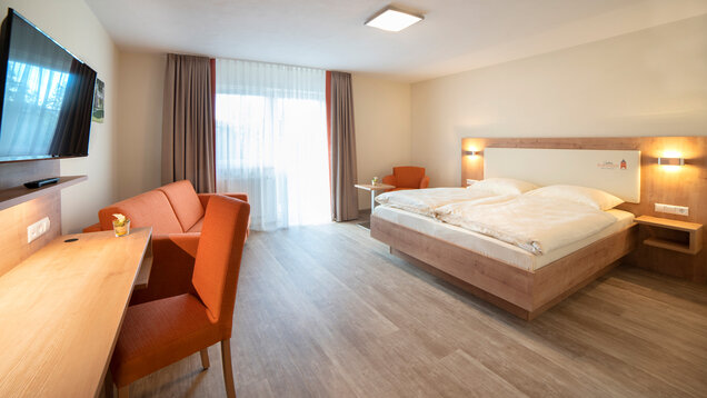 Doppelzimmer Komfort, Wischboden, Schreibtisch und Fernseher links, Balkon im Hintergrund, rechts Doppelbett