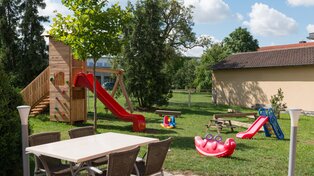 Bierarten, links ein Tisch im Hintergrund Außenspielbereich für Kinder mit Rutsche und Schaukel sowie Spielsachen